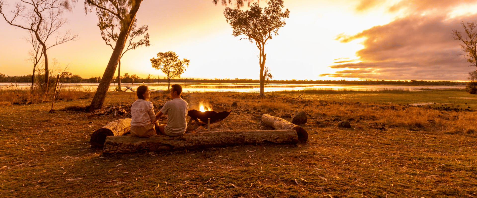 Woman And Man Sitting On Log Watching Sunset In Queensland Outback